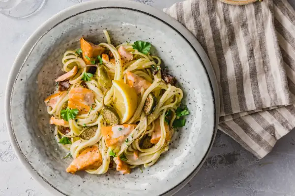 Ein Teller mit cremigen Nudeln mit Lachs, garniert mit Zitrone und Petersilie.