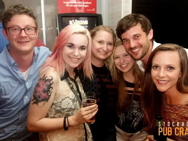 Glada vänner på en pub crawl i Stockholm. En kvinna med rosa hår håller ett glas öl.