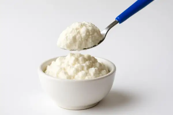 Ricotta fresca in una ciotola, con un cucchiaio che ne preleva una porzione. Un alimento leggero, ideale per chi controlla il colesterolo.