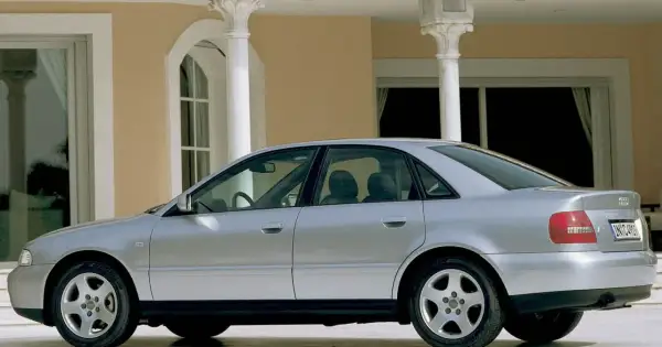 Srebrne Audi A4 B5 stoi przed eleganckim budynkiem z kolumnami.