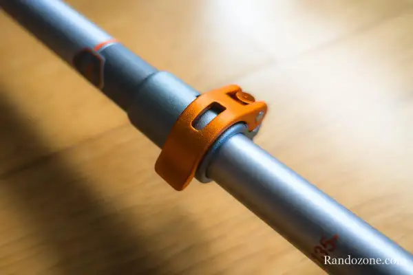 Gros plan sur le mécanisme de serrage orange d'un bâton de marche pliable ou télescopique, prêt pour l'aventure.