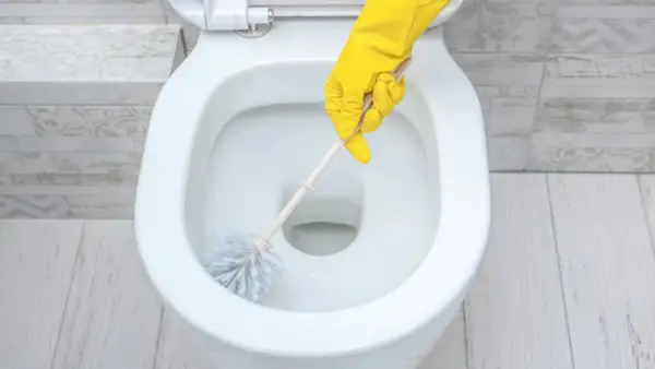 Main jaune nettoyant le tartre WC avec une brosse.