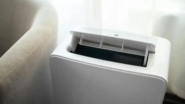 Nowoczesny klimatyzator bez jednostki zewnętrznej, z otwartą klapą wentylacyjną, obok jasnej kanapy.