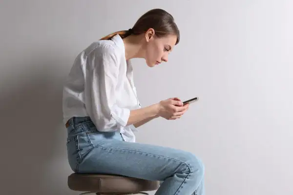 Frau mit schlechter Haltung, die auf ihr Handy schaut. Ihr Rücken ist gekrümmt, was zu einem Buckel am Nacken führt.