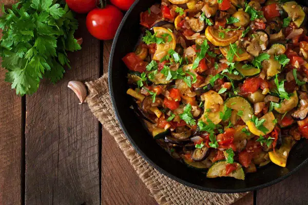 Padella piena di melanzane e zucchine saltate con pomodori e erbe fresche, un piatto colorato e saporito.