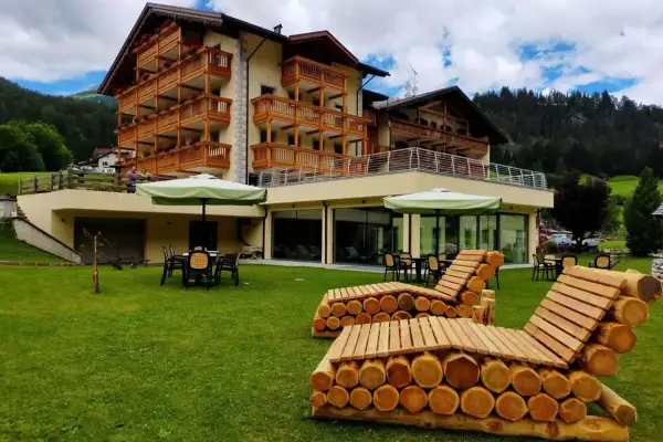 Hotel Dolomia Soraga: un'oasi di relax con vista sulle montagne. Panchine in legno e prato verde invitano al riposo.