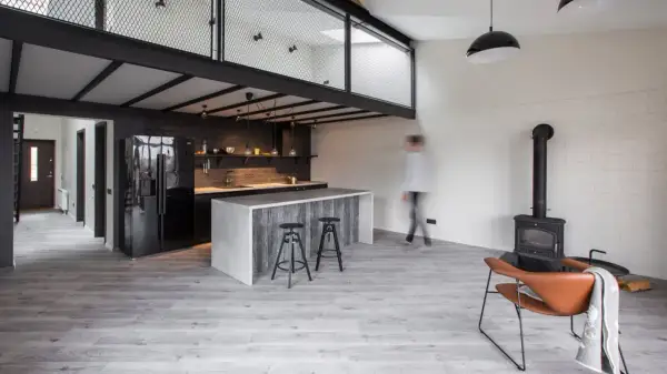 Nowoczesna kuchnia z wyspą i antresolą. Inspiracje dla loftowych wnętrz, gdzie industrialny styl łączy się z przytulnością kominka i wygodnym fotelem.