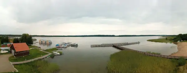 Widok na jezioro, gdzie wypływa roś. Widać pomosty, łodzie, pływające domki i plażę.
