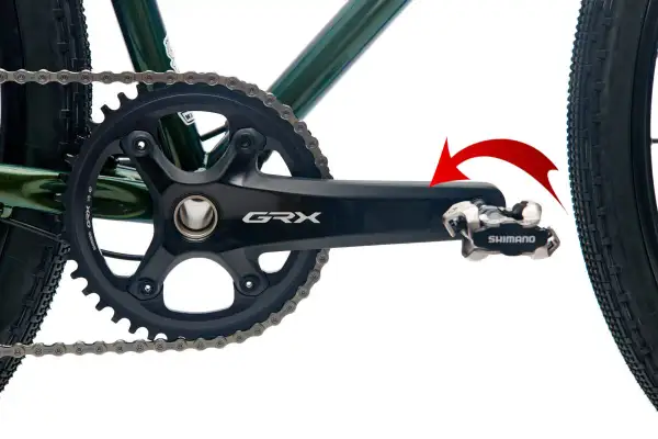 Czerwona strzałka pokazuje kierunek obrotu, by dowiedzieć się, jak odkręcić pedały w rowerze. Widoczny mechanizm korbowy Shimano GRX.