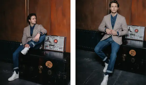 Junger Mann im lässigen Look: Sakko Herren sportlich zu Jeans, dazu weiße Sneaker. Ein Vintage-Tonbandgerät steht daneben.