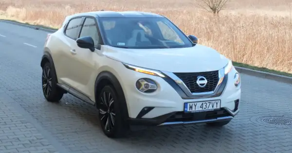 Biały Nissan Juke Sport z czarnym dachem i felgami, zaparkowany na kostce brukowej przy suchej trawie.