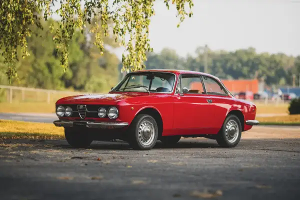 Klasyczny czerwony Alfa Romeo GT 1300 Junior, jeden z pięknych alfa romeo modele, stoi pod drzewem.