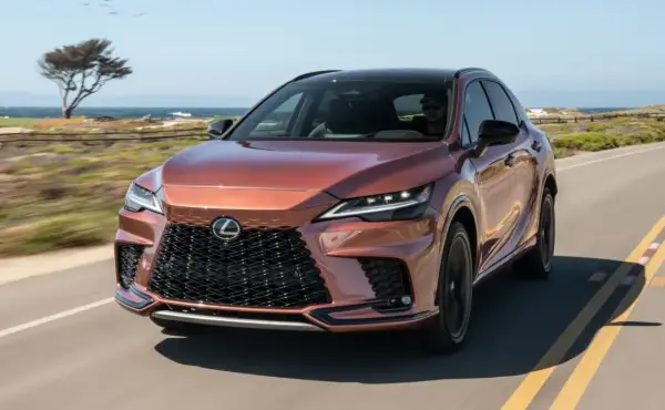 Miedziany Lexus RX 500h jedzie wzdłuż wybrzeża. Słońce odbija się od jego lśniącej karoserii.