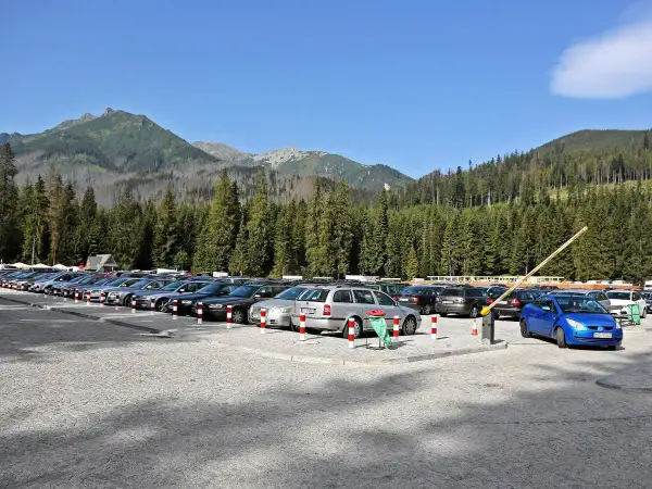 Parking Morskie Oko, cena za postój. Rząd samochodów na kamienistym parkingu, w tle las i góry.