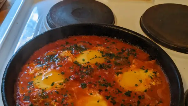 En varm och bubblande shakshuka med ägg i tomatsås, perfekt för ett mysigt frukostrecept.