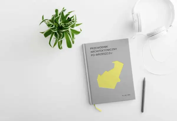 Przewodnik architektoniczny po Wrzeszczu, słuchawki i długopis na białym tle. Zielona roślina w doniczce.