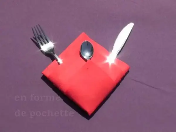 Pliage serviette Noël porte couvert en forme de pochette rouge, avec une fourchette, une cuillère et un couteau.