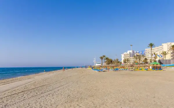 Amplia playa de la urbanización de Roquetas con sombrillas, tumbonas y edificios hoteleros al fondo.