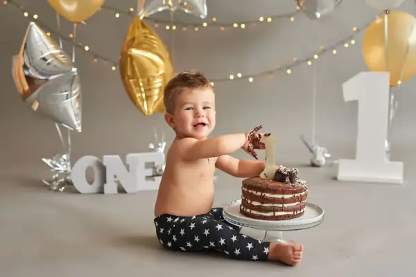 Uśmiechnięty chłopiec z czekoladą na rękach sięga po tort. Dekoracje i balony tworzą atmosferę przyjęcia z okazji pierwszych urodzin. Idealne cytaty na roczek dla dziewczynki i chłopca.