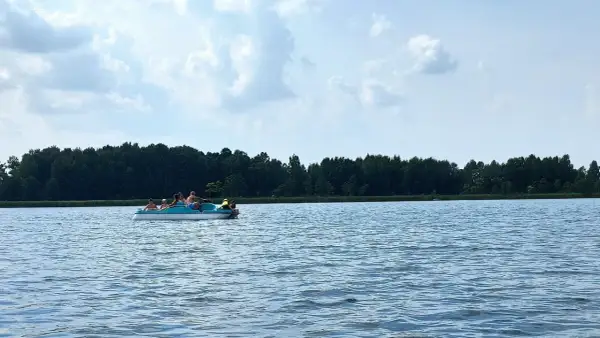 Rodzina pływa rowerkiem wodnym po spokojnym jeziorze Białka Lubelskie. W tle zielony las i błękitne niebo z chmurami.