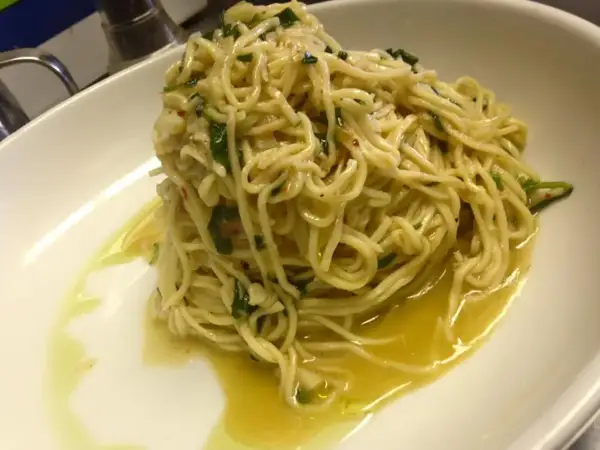 Un piatto di spaghetti aglio olio e peperoncino cremosi, conditi con prezzemolo fresco e un filo d'olio d'oliva.