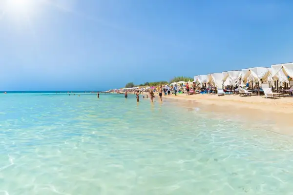 Spiaggia affollata in Puglia, con gente che fa il bagno nelle acque cristalline e si rilassa sotto i gazebo bianchi.