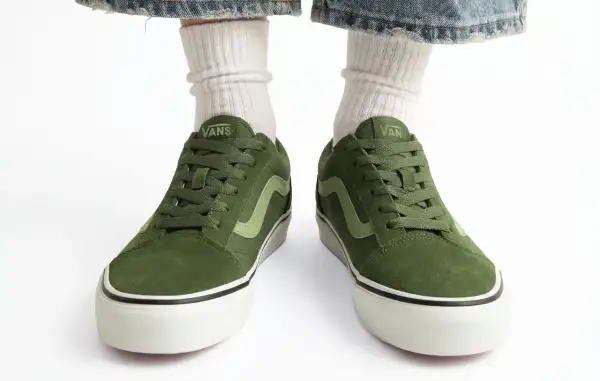 Zielone buty Vans na białym tle, widoczne od przodu, z nogawkami w białych skarpetkach i dżinsach.