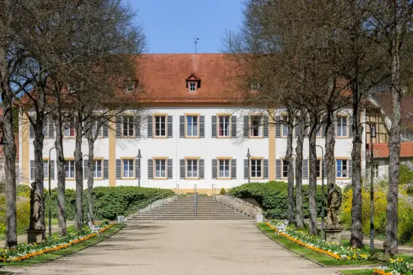 Prachtvolles Gebäude in Bad Bocklet, ideal für Ayurveda-Anwendungen. Ein Weg führt durch einen Garten mit Statuen und Blumen zum Eingang.