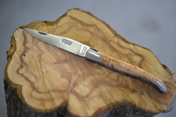 Navaja Laguiole artesanal, con mango de madera veteada y detalles plateados, reposa sobre un tocón de árbol.