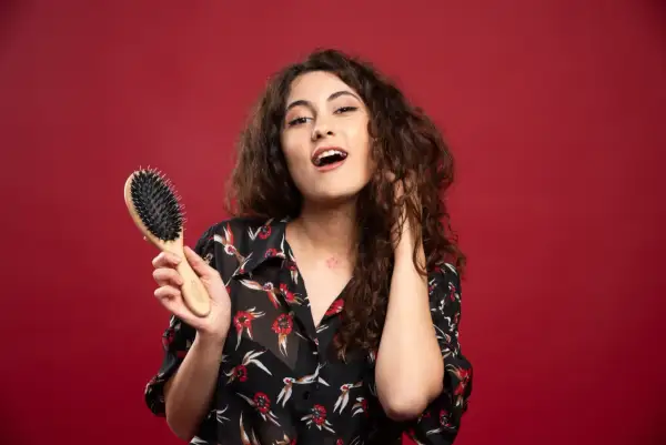 Ragazza con capelli ricci pettinati, tiene in mano una spazzola per capelli.