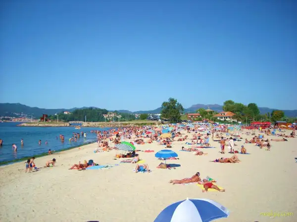 Día soleado en la playa Santa Marta de Baiona, con mucha gente disfrutando del mar y la arena bajo sombrillas.