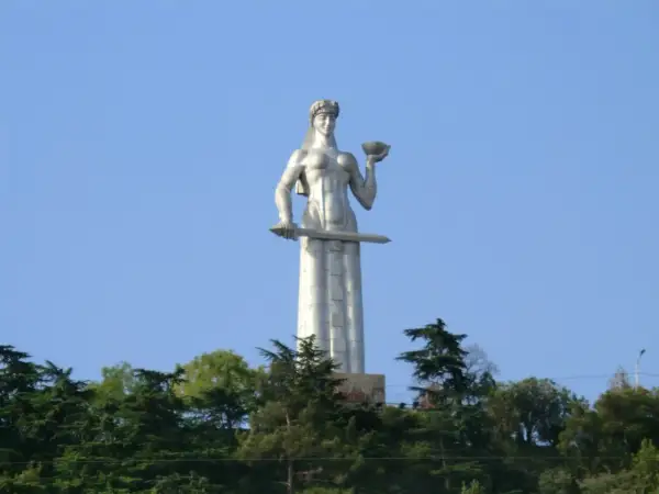 Matka Gruzja, symbol Tbilisi, trzyma miecz i puchar. Monumentalna postać wznosi się nad zielenią.