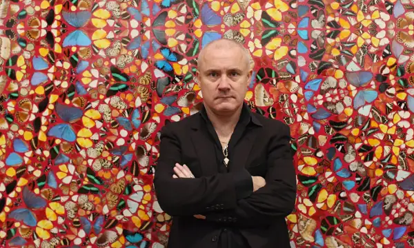 Damien Hirst stoi przed ścianą ozdobioną jego dziełami z motyli.