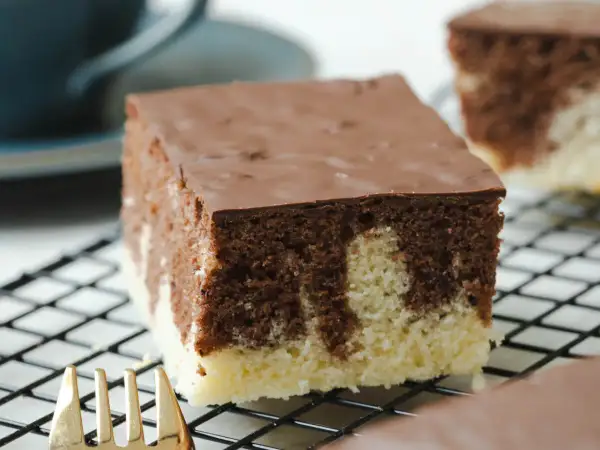 Ein Stück saftiger Marmorkuchen vom Blech mit Schokoladenglasur auf einem Kuchengitter.