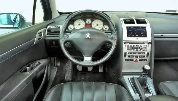 Wnętrze Peugeot 407 2.0 HDI. Widok na deskę rozdzielczą, kierownicę, dźwignię zmiany biegów i siedzenie kierowcy.