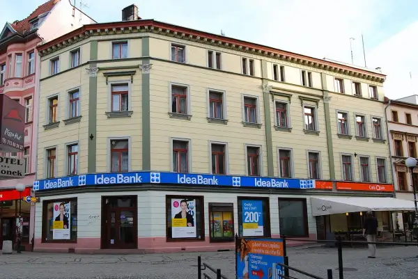 Elegancki budynek z szyldami Idea Bank i Cafe Qbek. W witrynach banku reklamy kredytów i usług.
