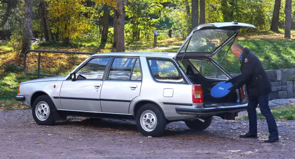 Man lastar en blå frisbee i bakluckan på en silverfärgad Renault 18 kombi i höstlandskap.