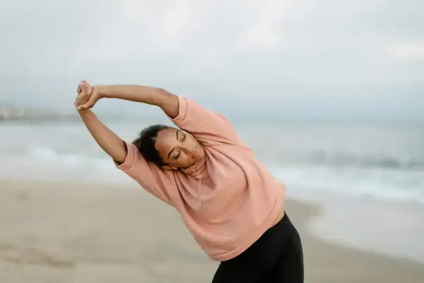 Femme en posture qi gong, s'étirant sur la plage au lever du soleil.
