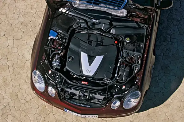 Silnik V6 om642 Mercedesa E-klasy, z otwartą maską, na tle spękanej ziemi.