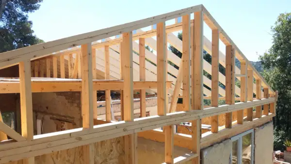 Estructura de madera para casa en construcción, con vigas y pilares de madera a la vista bajo un cielo azul.