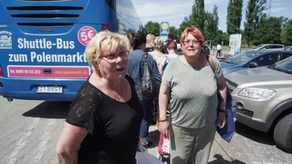 Zwei Frauen warten auf den Shuttle-Bus zum Polenmarkt. Der blaue Bus wirbt mit "5€ Fahrpreis".