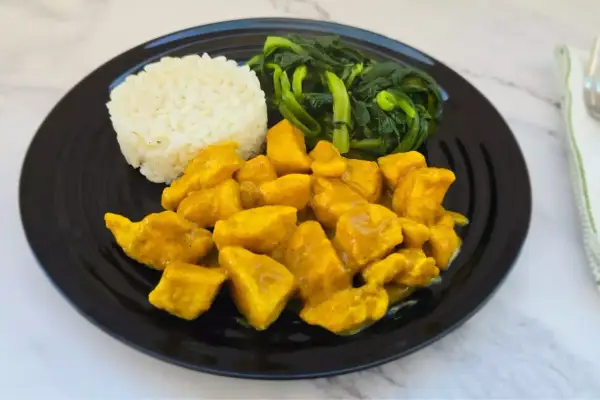 Piatto di pollo al curry con latte di cocco, riso bianco e verdure verdi saltate.