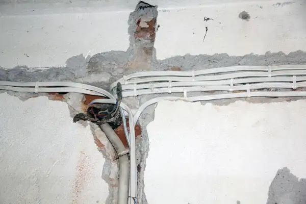 Widoczne przewody elektryczne w peszlach, częściowo ukryte w bruzdach w ścianie. Instalacja aluminiowa w trakcie prac.