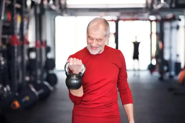 Ein älterer Mann trainiert mit einer Kettlebell. Ein guter Trainingsplan für Krafttraining ab 60 Jahren hält ihn fit.