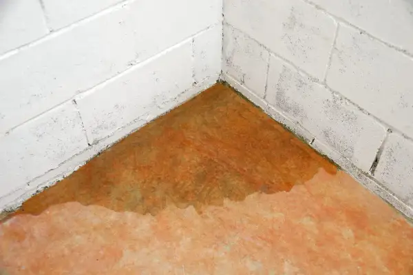 Ecke eines Kellers mit Wasser auf dem Boden und an den weißen Ziegelwänden. Ein Wasserschaden im Keller? Was tun?