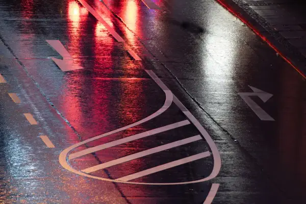 Nasse Straße mit roten und weißen Lichtreflexionen. Pfeile auf dem Asphalt zeigen die Fahrtrichtung an, wie bei einer anhalteweg formel.