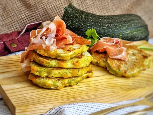 Deliciosas tortillitas de calabacín apiladas, coronadas con jamón serrano. Un plato fresco y sabroso.