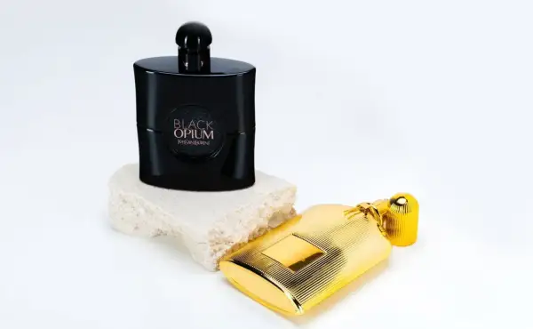 Elegancki flakon Black Opium 90 ml na kamiennej podstawie obok złotego flakonu.