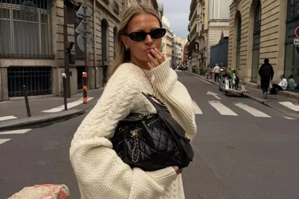 Mujer con suéter tejido y bolso negro, paseando por una calle parisina con estilo bohemio.