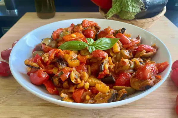 Caponata ricetta semplice: melanzane, peperoni e pomodorini cotti insieme, guarnita con basilico fresco. Un contorno saporito e colorato.